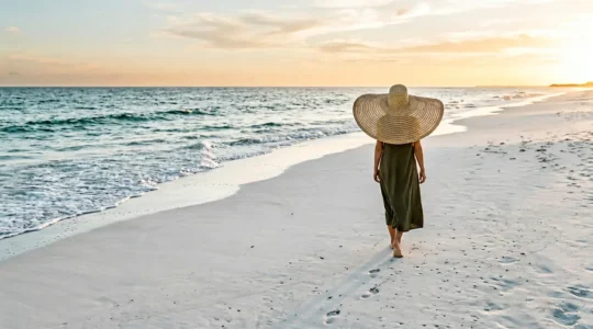 Vue large d'une silhouette féminine portant un chapeau XXL à larges bords sur une plage ensoleillée, créant une ombre protectrice