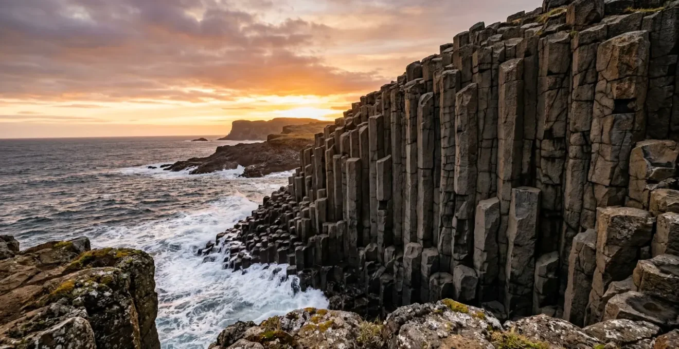 Colonnes basaltiques hexagonales monumentales émergeant d'une falaise côtière au coucher du soleil