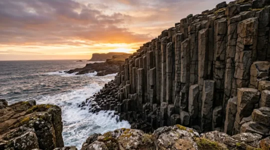 Colonnes basaltiques hexagonales monumentales émergeant d'une falaise côtière au coucher du soleil