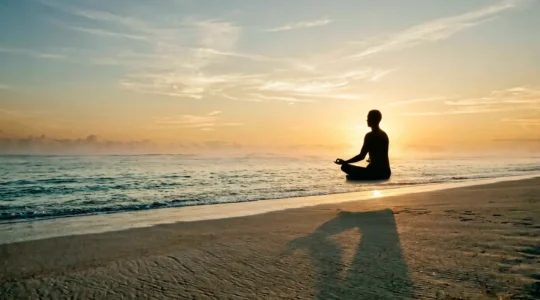 Personne en posture de méditation face à l'horizon océanique au lever du soleil