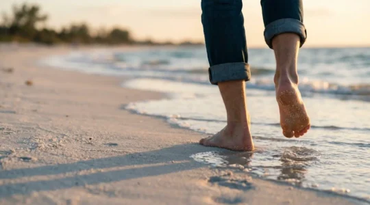 Pieds nus marchant sur du sable fin blanc au bord de l'eau avec des vagues douces