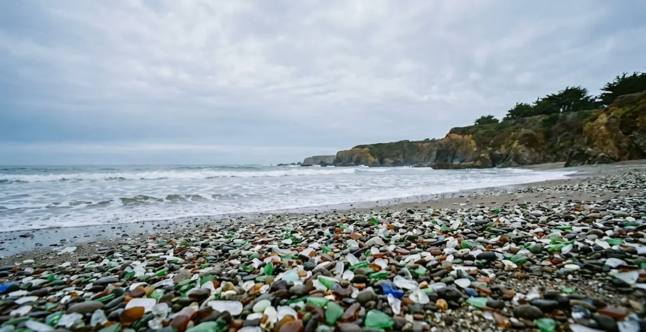 Fragments de verre de mer colorés polis par l'océan sur une plage, témoignage visuel de la transformation de déchets en beauté naturelle