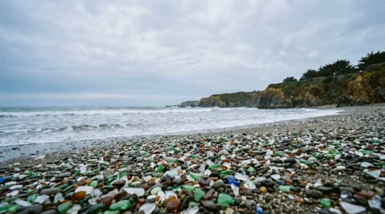 Fragments de verre de mer colorés polis par l'océan sur une plage, témoignage visuel de la transformation de déchets en beauté naturelle