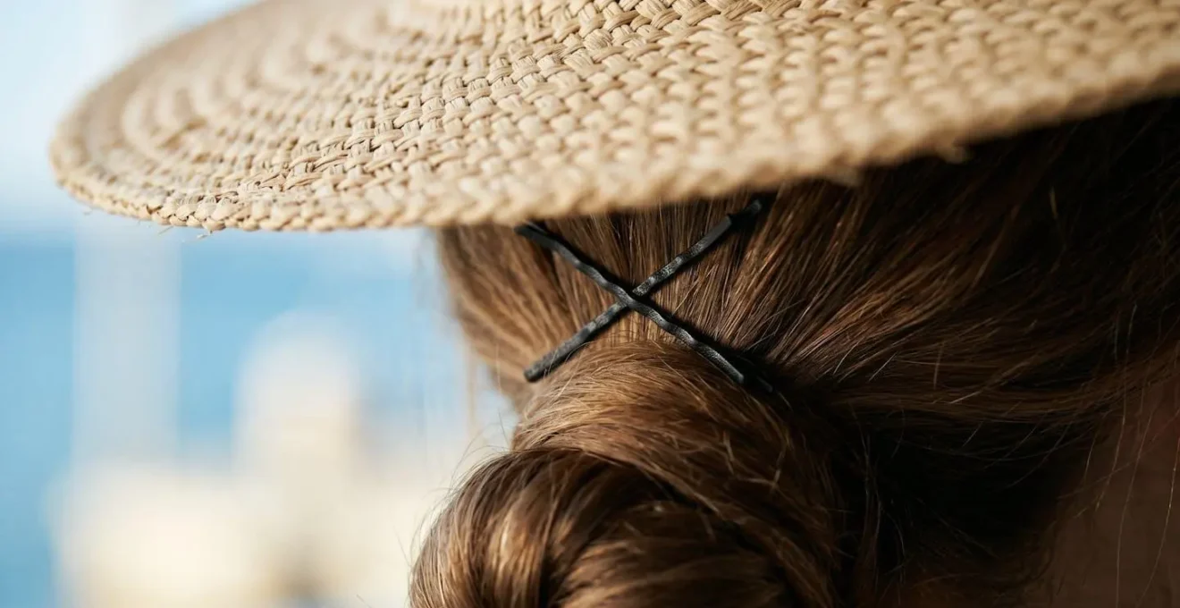 Gros plan sur une fixation discrète d'un chapeau de paille avec des épingles à chignon croisées sur une coiffure basse