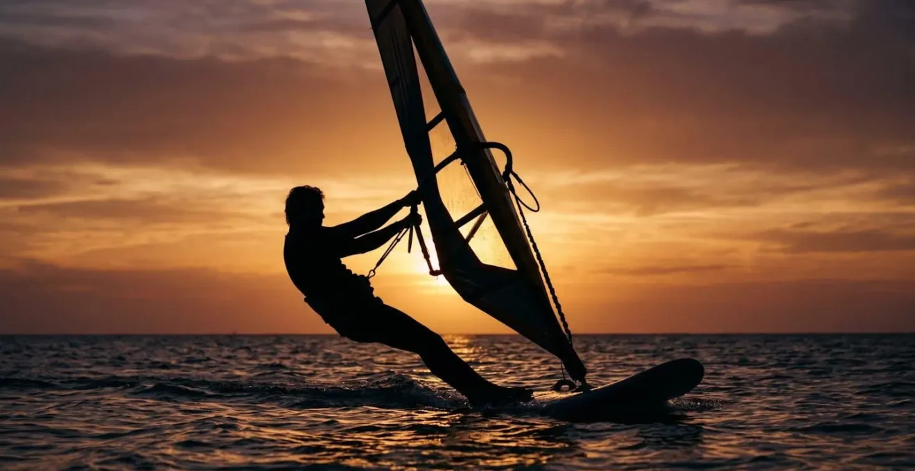 Silhouette d'un véliplanchiste en contre-jour utilisant son poids corporel comme contrepoids face à la voile